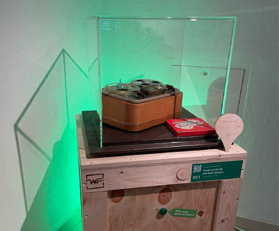 Vitrine mit einem Grundig Tonbandgerät im Holzkorpus.